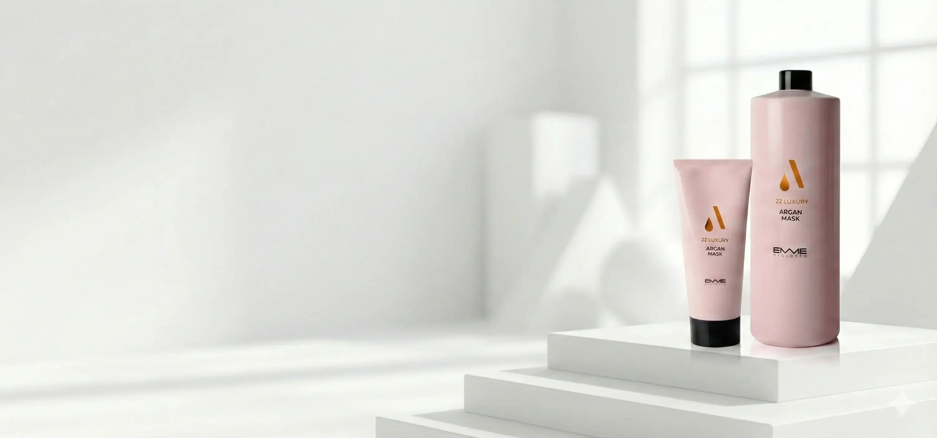 Emme Diciotto 22 Luxury Argan Mask in a pink squeeze tube and large bottle, displayed on a white tiered podium in a bright minimalist room.1621243260e1af0c20-0